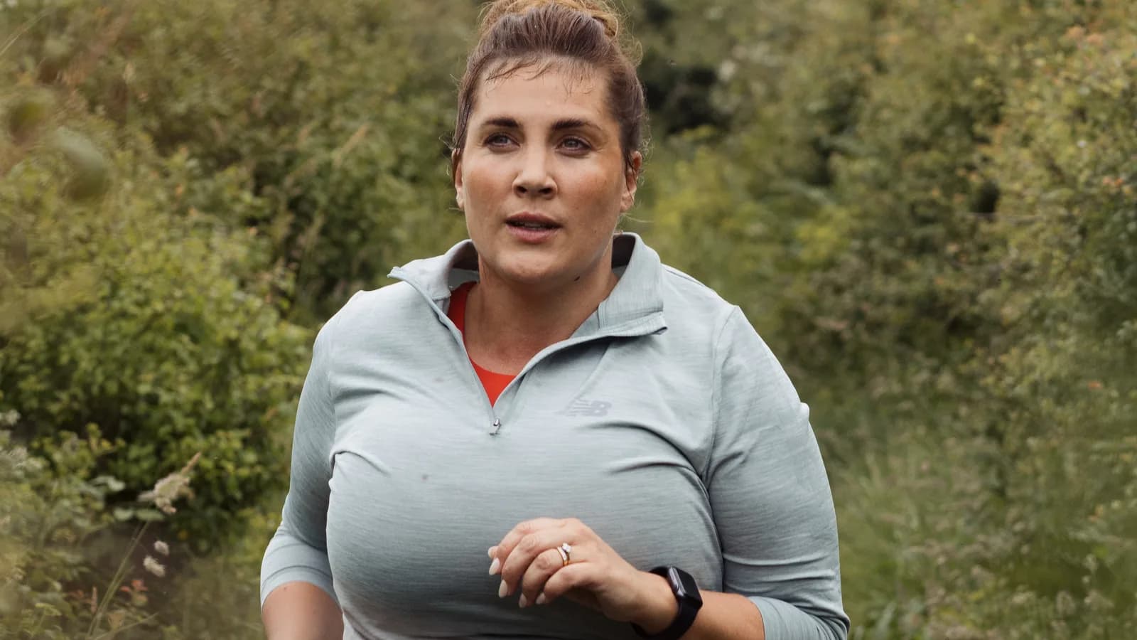 Kobieta w sportowym stroju biegnie po łące w pochmurny dzień